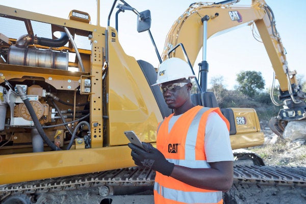 Man looking at his phone next to a Cat 326 Excavator with a grapple