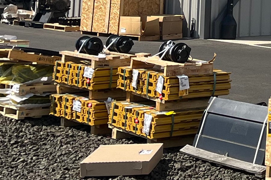 Pallets of steel tracks, rollers, buckets, and ground-engaging tools.