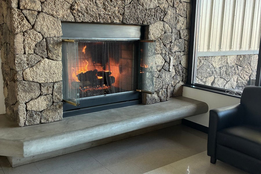 A fire burns inside a stone fireplace with built-in bench beside a leather chair