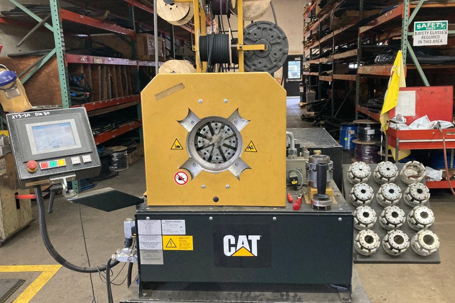 a computerized Cat hose crimper in front of spools of capped hydraulic lines in the Eugene parts warehouse