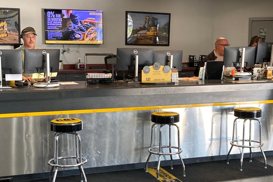 Three parts professionals behind the parts counter with customer seating and finance specials on a monitor in the background