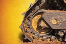 worn undercarriage of a cat dozer on an orange to yellow gradient background