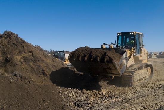 A 973 crawler loader with a bucket carries fill dirt on the job site