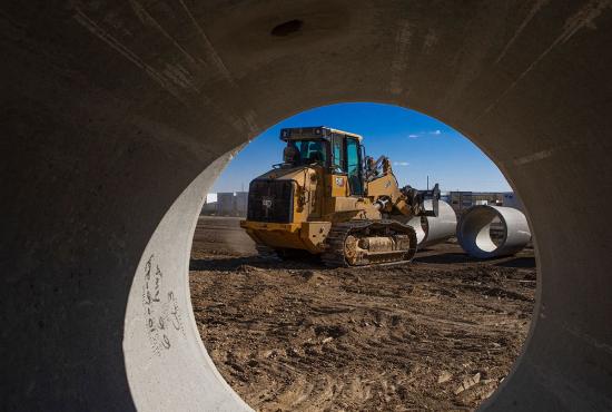 973 crawler loader with a quick coupler picking up sewer pipe, as seen through a concrete pipe