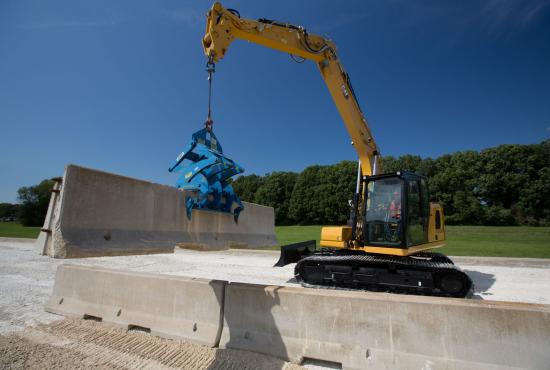 Cat 313 hydraulic excavator lifting a concrete barrier at a worksite.